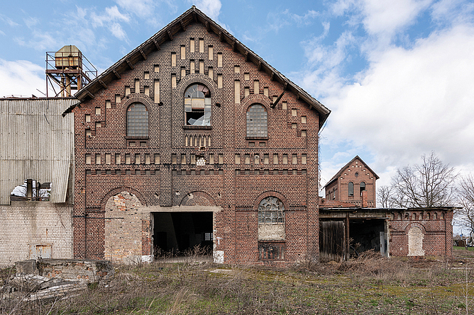Altes Backsteingebäude mit beschädigter Fassade und offenen Fenster- und Türöffnungen.