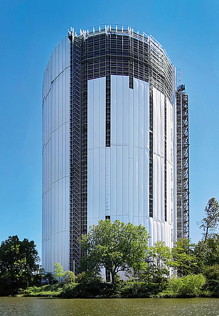 Eingerüsteter Gasometer, teilweise mit weißen Planen behangen.
