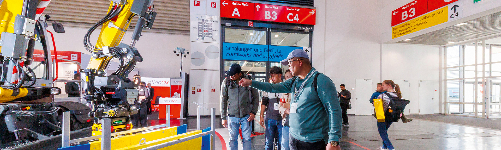 Besucher am Messestand der BG BAU BAU auf der bauma 2025 Mehrere Personen schauen interessiert den Bagger am Messestand an.
