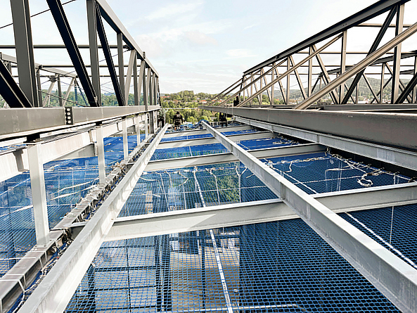 Stahlkonstruktion in der Höhe, in die ein blaues Arbeitsplattformnetz eingespannt ist. 