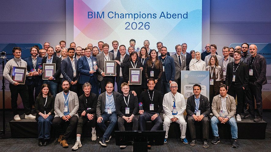 Gruppenfoto von rund 50 Personen auf einer Bühne vor einer Leinwand mit der Aufschrift „BIM Champions Abend 2026“; mehrere Personen halten gerahmte Auszeichnungen.