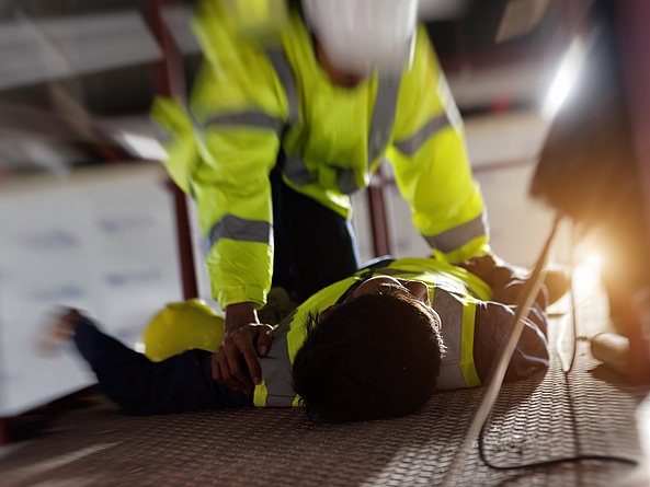 Ein Bauarbeiter leistet einem anderen Bauarbeiter bei einem Arbeitsunfall Erste Hilfe.