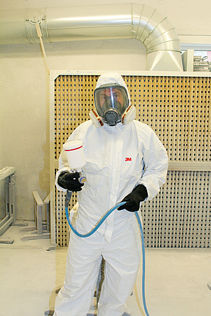 Geschulter Beschäftigter beim Lackieren mit Polyurethan-Lack: Er trägt Schutzanzug, Atem-, Gesichts- und Gehörschutz sowie Arbeitshandschuhe