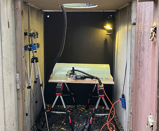 Blick in einen geöffneten Betonschacht mit Messtechnik auf einem Arbeitstisch sowie einem Stativ und Beleuchtung.