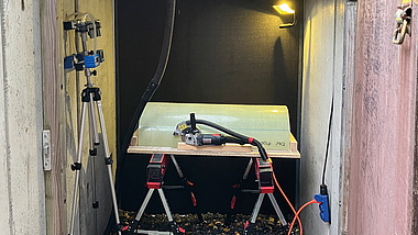 Blick in einen geöffneten Betonschacht mit Messtechnik auf einem Arbeitstisch sowie einem Stativ und Beleuchtung.