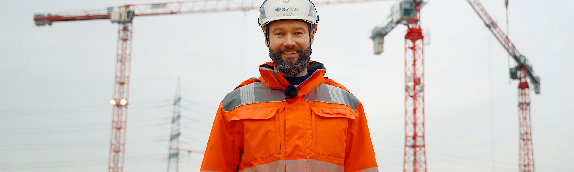 Titelbild des Videos "9 lebenswichtige Regeln im Hochbau": Marc Schuler steht auf einer Baustelle vor drei Kränen.