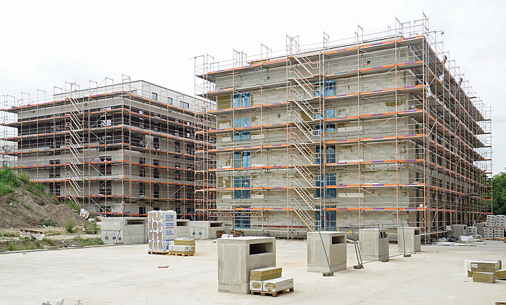 Zwei mehrgeschossige Gebäude im Rohbau, vollständig eingerüstet, auf einer Baustelle.
