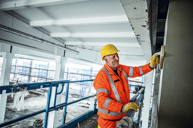 Ein Mann auf einem Hubsteiger verteilt am Deckenrand das aufgetragene Material.