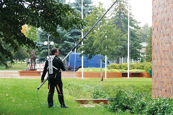 Einsatz des Teleskopstangen-Systems mit Rucksack bei der Fassadenreinigung Ein Mann nutzt bei der Fassadenreinigung ein Teleskopstangen-System mit Rucksack für die Zufuhr von Reinwasser.