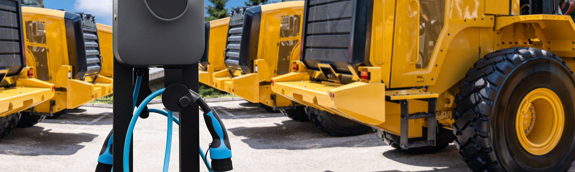 Mehrere Radlader stehen um eine Ladesäule herum.