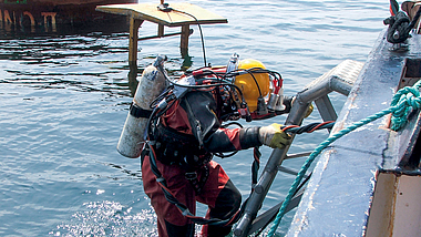 gewerbliches Tauchen Gewerblicher Taucher an einer Bootsleiter auf einer Wasserbaustelle.