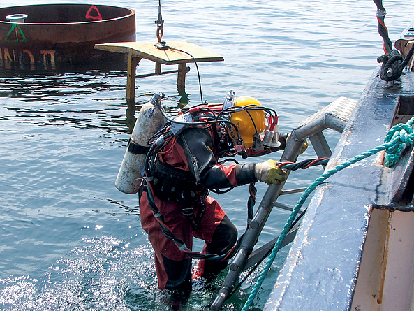 Gewerblicher Taucher an einer Bootsleiter auf einer Wasserbaustelle.