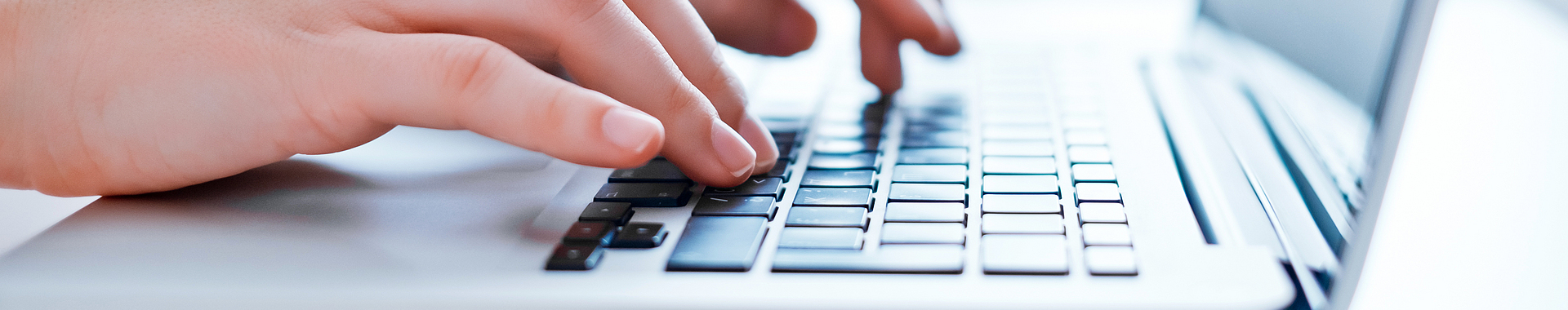 Zwei Hände tippen etwas auf einer Tastatur eines Laptops.