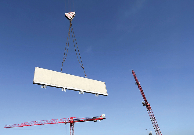 Betonfertigteil hängt an einem Kran vor blauem Himmel.