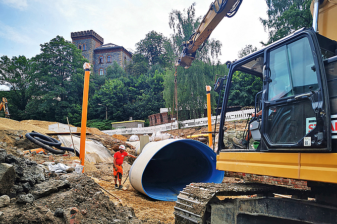 Baggertechnik ist ausreichend, um die GFK-Maulprofile 3.200 × 2.000 auf der Baustelle zu bewegen. Ein Bauarbeiter mit PSA berührt ein ovales Rohr, das von einem kleinen Bagger auf dem Boden der Baugrube abgesetzt wird.