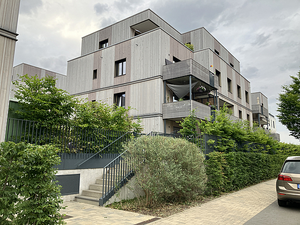 Neu gebautes Wohngebäude mit Balkon und verwitterter Holzfassade.