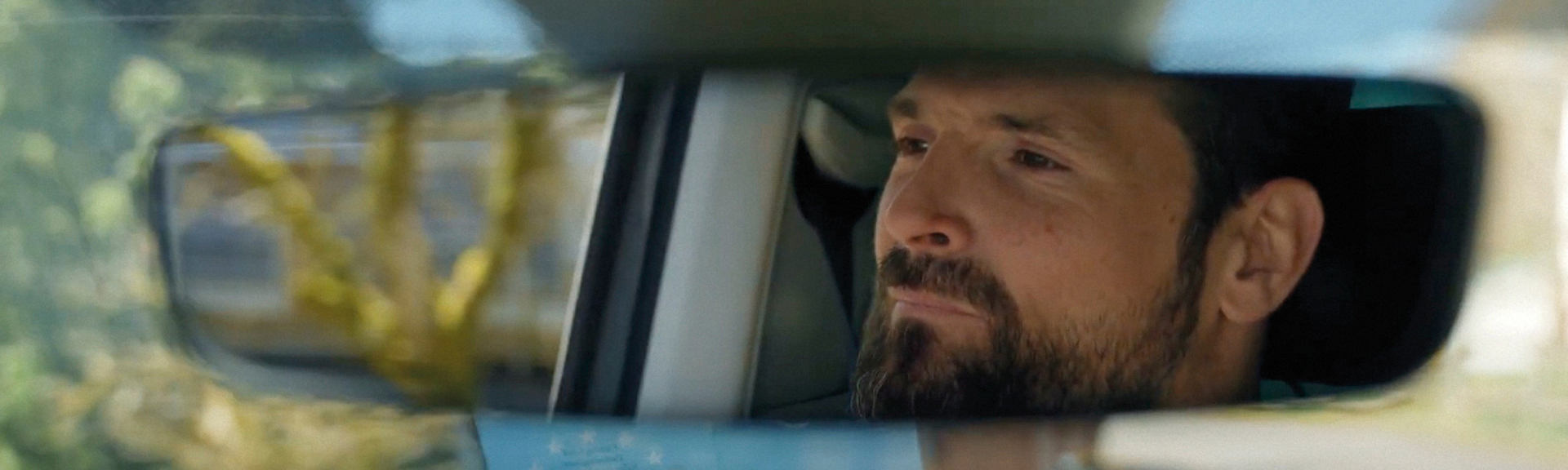 Das Gesicht eines Mannes ist im Rückspiegel eines Autos zu sehen. Er blickt konzentriert nach vorn.