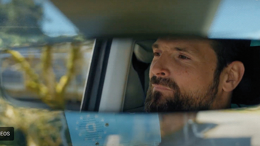 Das Gesicht eines Mannes ist im Rückspiegel eines Autos zu sehen. Er blickt konzentriert nach vorn.