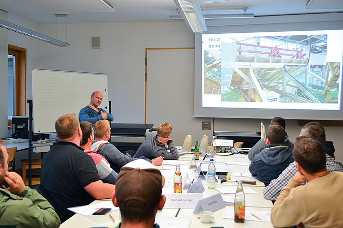 Fachkunde Absturzprävention: Theorie und praxisnahe Lösungen Eine Gruppe von Seminarteilnehmenden folgt einem Vortrag in einem Seminarraum mit Großbildschirm.