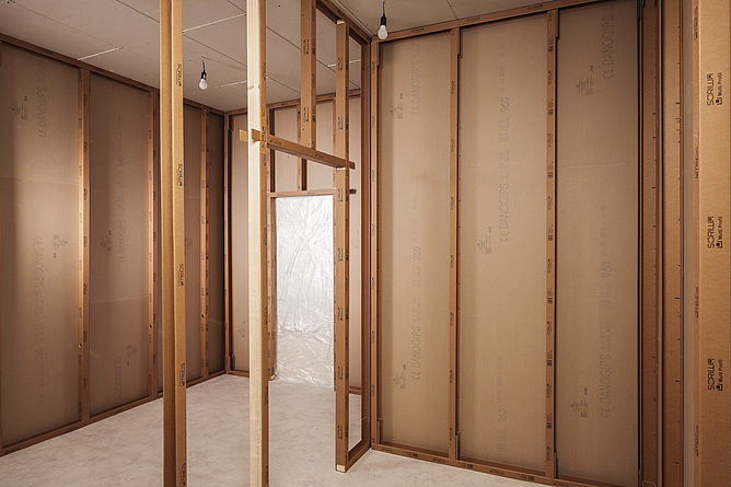 Innenansicht eines Raums im Holzrahmenbau mit freiliegenden Holzständern und Wandplatten im Rohbau.