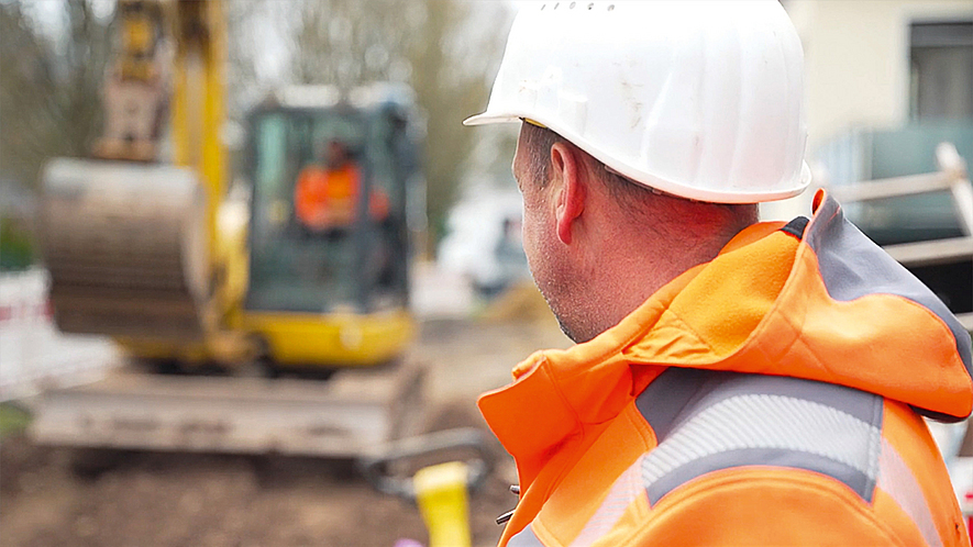 Baustelle mit Bagger Ein Bauarbeiter steht vor einem Bagger auf der Baustelle.