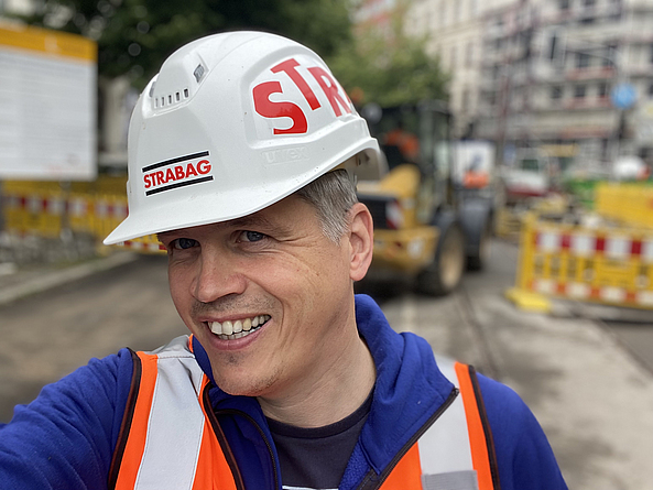 Mann mit Schutzhelm, auf dem STRABAG steht, und Warnweste.