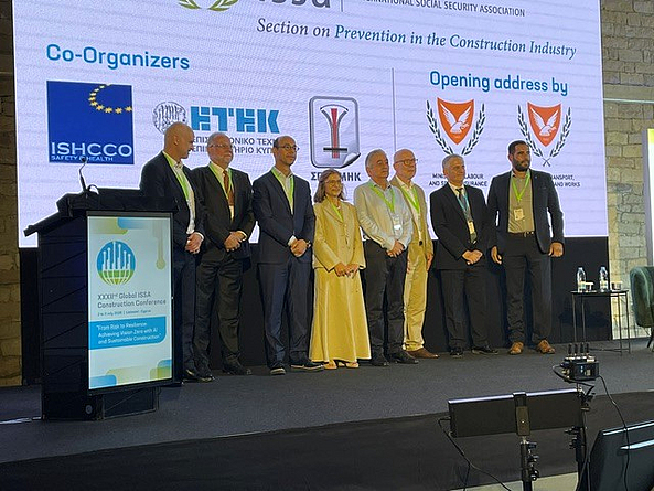 Sieben Männer und eine Frau stehen auf einem Podium vor einer Präsentationswand.