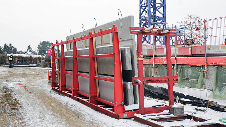 Rotes Transportgestell mit verschiedenen Betonfertigteilen auf einer Baustelle.