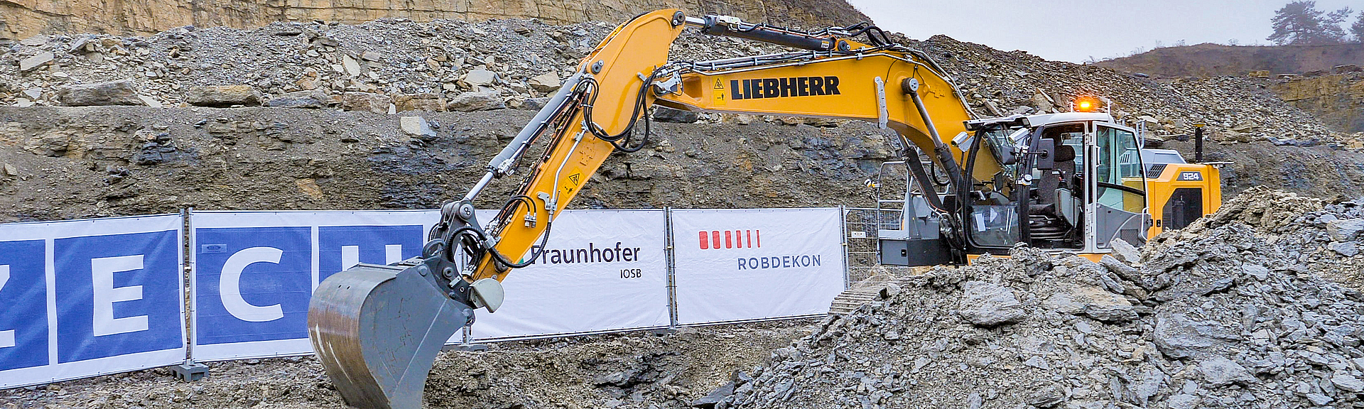 Gelber (autonomer) Bagger ohne Bedienperson baggert in einem Steinfeld.