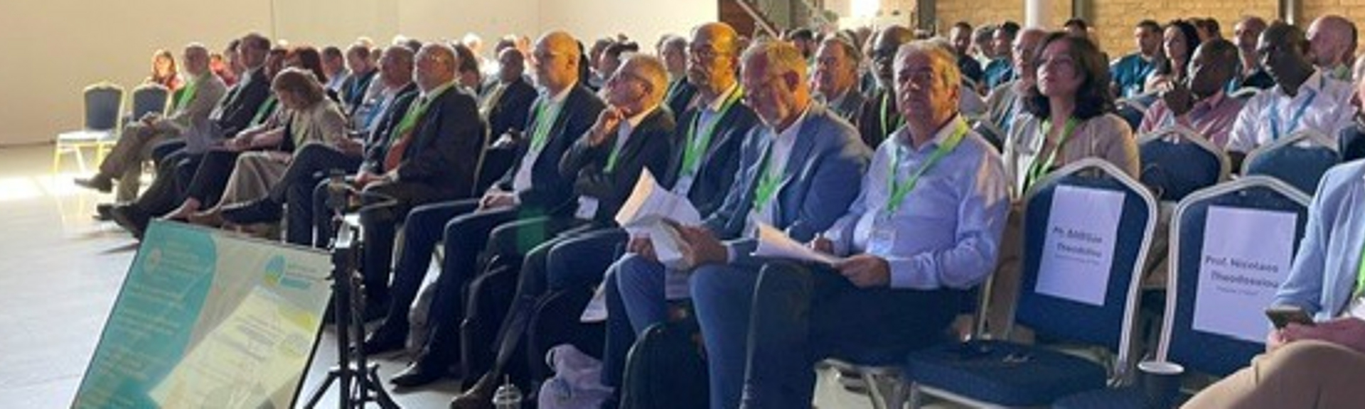 Große Anzahl von Menschen, die in einer Halle mit mehren Reihen auf Stühlen sitzen.