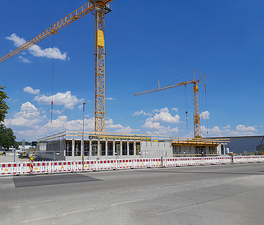 Baustelle neues Polizeigebäude Kaufbeurem Abgezäunte Baustelle mit zwei Kränen an einer Straße, der untere Teil eines Rohbaus steht bereits.
