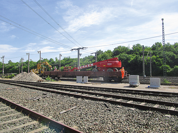 Zwei Bauarbeiter auf einem Güterwagen in einer Gleisbaustelle.