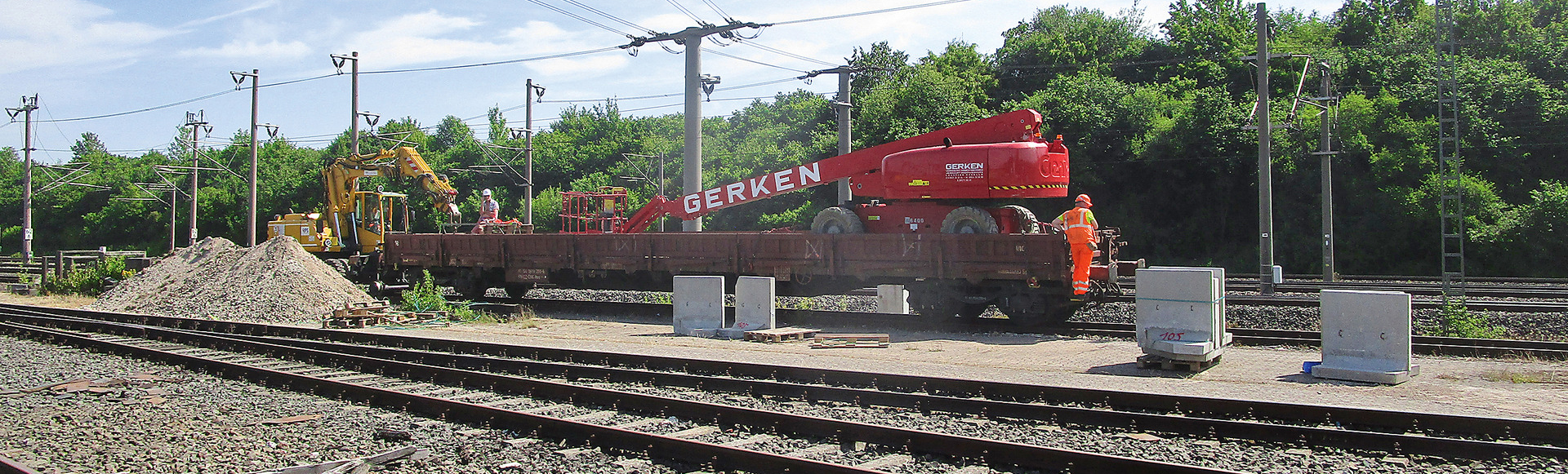 Zwei Bauarbeiter auf einem Güterwagen in einer Gleisbaustelle.