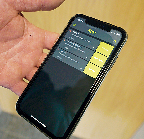 Smartphone in einer Hand, das im Display die App für das digitale Schließsystem zeigt.