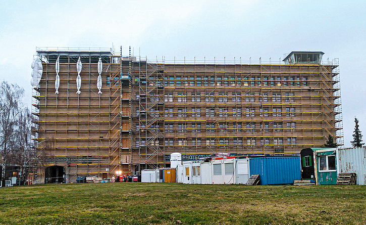 Energetische Sanierung des westlichen Kopfgebäudes des historischen Flughafens Tempelhof. Vor der Fassade stehen Gerüste und mehrere Baucontainer.