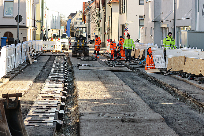 In die Straßen werden Spulen (Coils) eingelegt. Verlegung von Spulen in einer Straße. Im Hintergrund mehrere Straßenbauarbeiter neben einem Baufahrzeug.