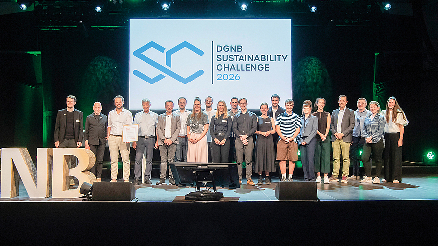Gruppenfoto von rund 30 Personen auf einer Bühne vor einer Leinwand mit dem Logo und Schriftzug „DGNB Sustainability Challenge“.