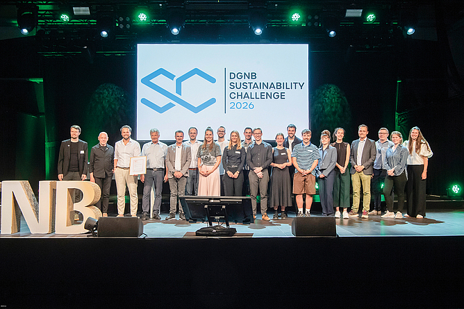 Gruppenfoto von rund 30 Personen auf einer Bühne vor einer Leinwand mit dem Logo und Schriftzug „DGNB Sustainability Challenge“.