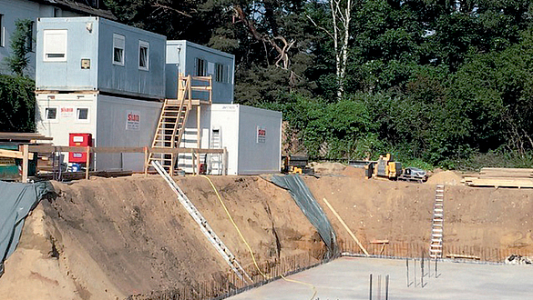Unzulässige Containerauflast am Böschungsrand Aufeinander gestapelte Container am Böschungsrand einer großen Baugrube, in welche Leitern führen und in deren Grund Bewehrungseisen herausragen.