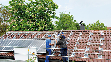 Drei Männer montieren eine Photovoltaik-Anlage auf einem Dach. 