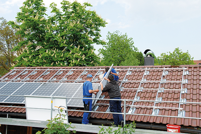 Drei Männer montieren eine Photovoltaik-Anlage auf einem Dach. 