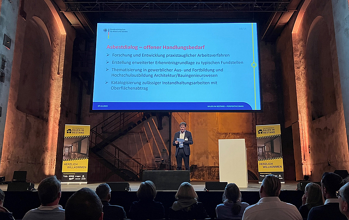 Dr. Georg Hilpert eröffnete den Fachkongress mit einem Vortrag über die künftige Gefahrstoffverordnung. Ein Mann steht auf einer Bühne in einem großen Saal und hält einen Vortrag.