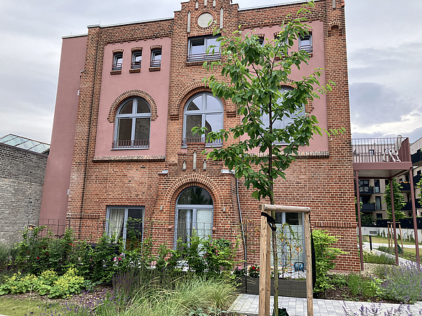 Saniertes Backsteingebäude mit neuen Fenstern in einem begrünten Hof.