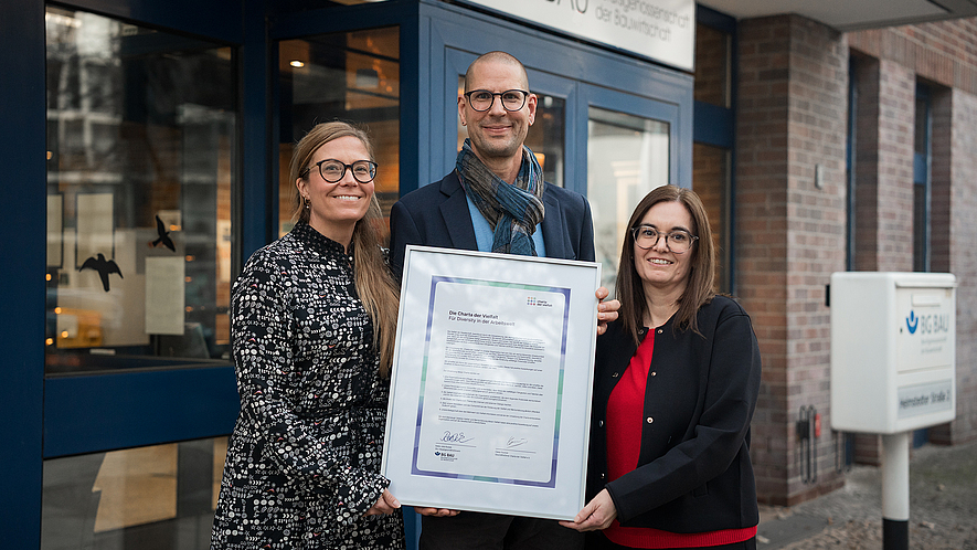 Die stellvertretende Hauptgeschäftsführerin der BG BAU Katia-Julia Rostek (links im Bild) mit Alexandra Schlosser, der Inklusionsbeauftragten der BG BAU und Thomas Kampe aus dem Referat Organisationsentwicklung halten die Beitrittsurkunde „Die Charta der Vielfalt“.