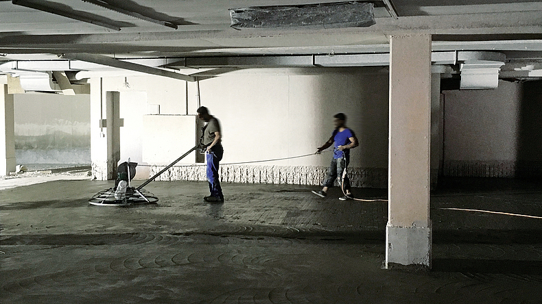 Beim Einsatz von Elektroglättern mit Kabel muss das Stromkabel von einer weiteren Person nachgeführt werden. Ein Mann steuert einen Elektroglätter, ein weiterer führt das dazu gehörige Kabel.