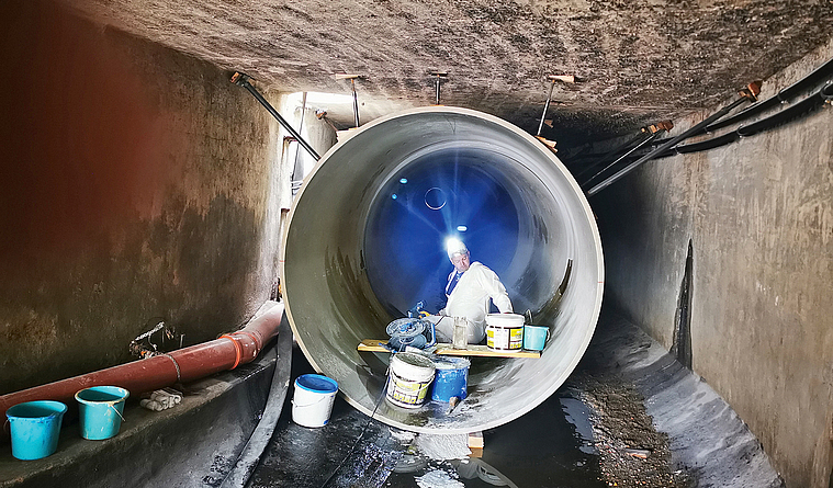  In einem großen Rohr sitzt ein Mann mit Stirnlampe und Eimern und verfüllt etwas.