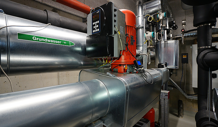 Detailbild der Wärmepumpenanlage, welches das Grundwasserohr und die Bedienstation zeigt.