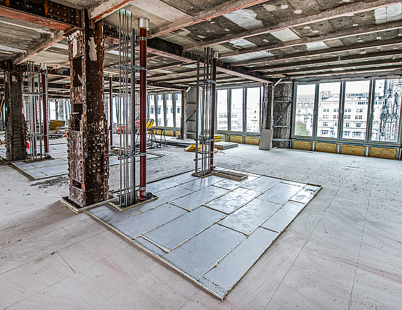 In den Bereichen der späteren Badezimmer wurden die Estrichelemente fermacell® Powerpanel TE eingesetzt. Baustelle in einem Gebäude, in dem Decken- und Fußbodenarbeiten durchgeführt werden. An einem Pfeiler wurden ein Rechteck mit beschichteten Platten ausgelegt.