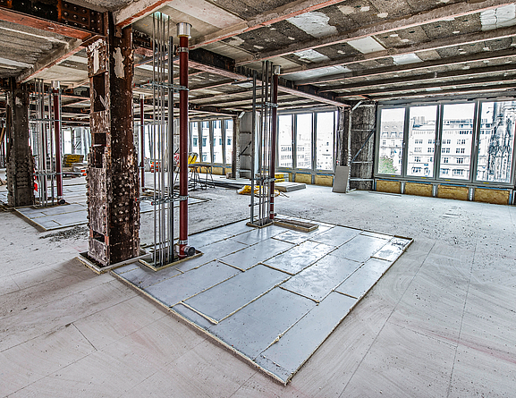 Baustelle in einem Gebäude, in dem Decken- und Fußbodenarbeiten durchgeführt werden. An einem Pfeiler wurden ein Rechteck mit beschichteten Platten ausgelegt.