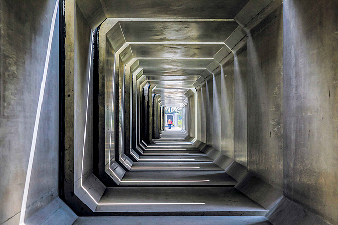 Ein Blick in das Innere eines Betonkanals. Am anderen Ende steht eine Person.